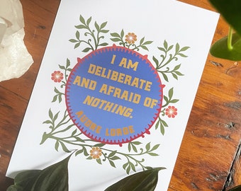 May include: A white card with a blue circle and gold text that reads "I am deliberate and afraid of nothing." The circle is surrounded by green leaves and orange flowers.