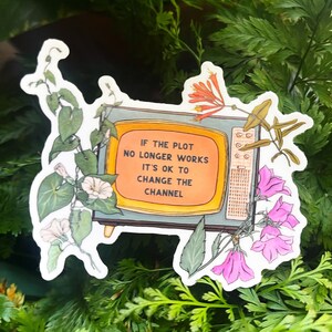 May include: A sticker featuring a vintage television with the text "IF THE PLOT NO LONGER WORKS IT'S OK TO CHANGE THE CHANNEL." The sticker is decorated with floral and vine illustrations in green, pink, and orange.