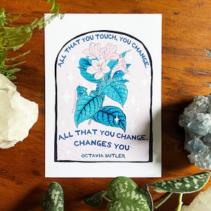 Peut inclure: Une illustration d'une fleur rose et bleue avec la citation "Tout ce que vous touchez, vous changez. Tout ce que vous changez, vous change. Octavia Butler" imprim&eacute;e sur un fond blanc.