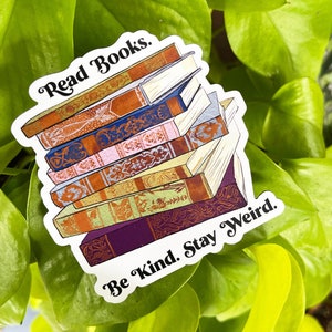 Puede incluir: Una pegatina blanca con una pila de libros ilustrados de colores. La pegatina tiene el texto "Read Books. Be Kind. Stay Weird."