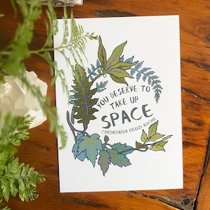 May include: A white card with a green leafy wreath design and the text "You deserve to take up space" with the author's name "Chimamanda Ngozi Adichie" below.