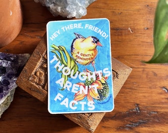 Könnte beinhalten: Ein Aufkleber mit blauem Hintergrund und dem Text "HEY THERE, FRIEND!" und "THOUGHTS AREN'T FACTS." Er zeigt einen gelben Vogel mit rotem Schnabel und den Worten "A GENTLE REMINDER." Der Aufkleber befindet sich auf einer Holzbox.