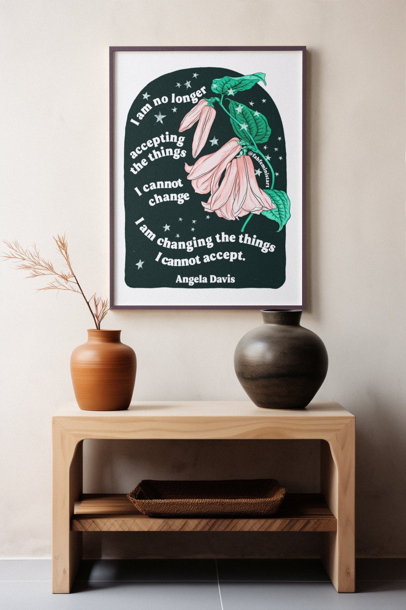 May include: A framed print with a black background and a pink flower with green leaves. The print features the text "I am no longer accepting the things I cannot change. I am changing the things I cannot accept. Angela Davis."