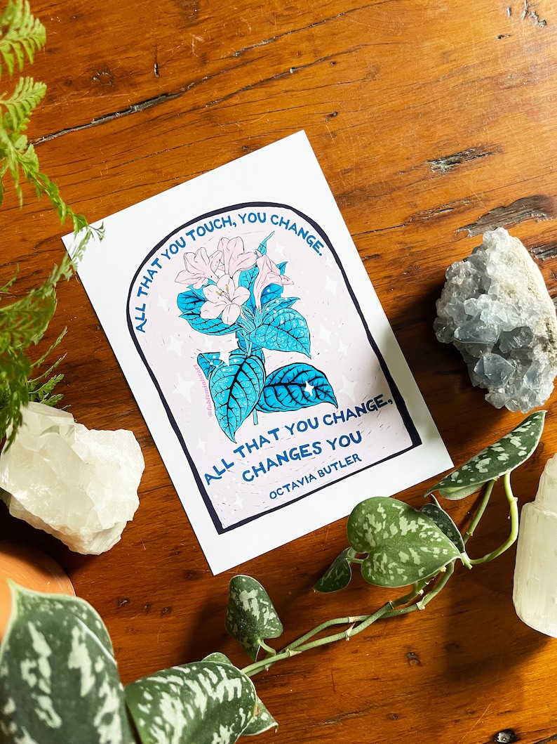 Peut inclure: Une carte blanche avec une illustration de fleur rose et du texte bleu qui dit "Tout ce que vous touchez, vous changez. Tout ce que vous changez, vous change. Octavia Butler."
