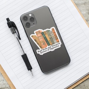 May include: A sticker with a stack of vintage books and the text "Read Books and Dismantle Systems of Oppression". The sticker is on a gray phone case.