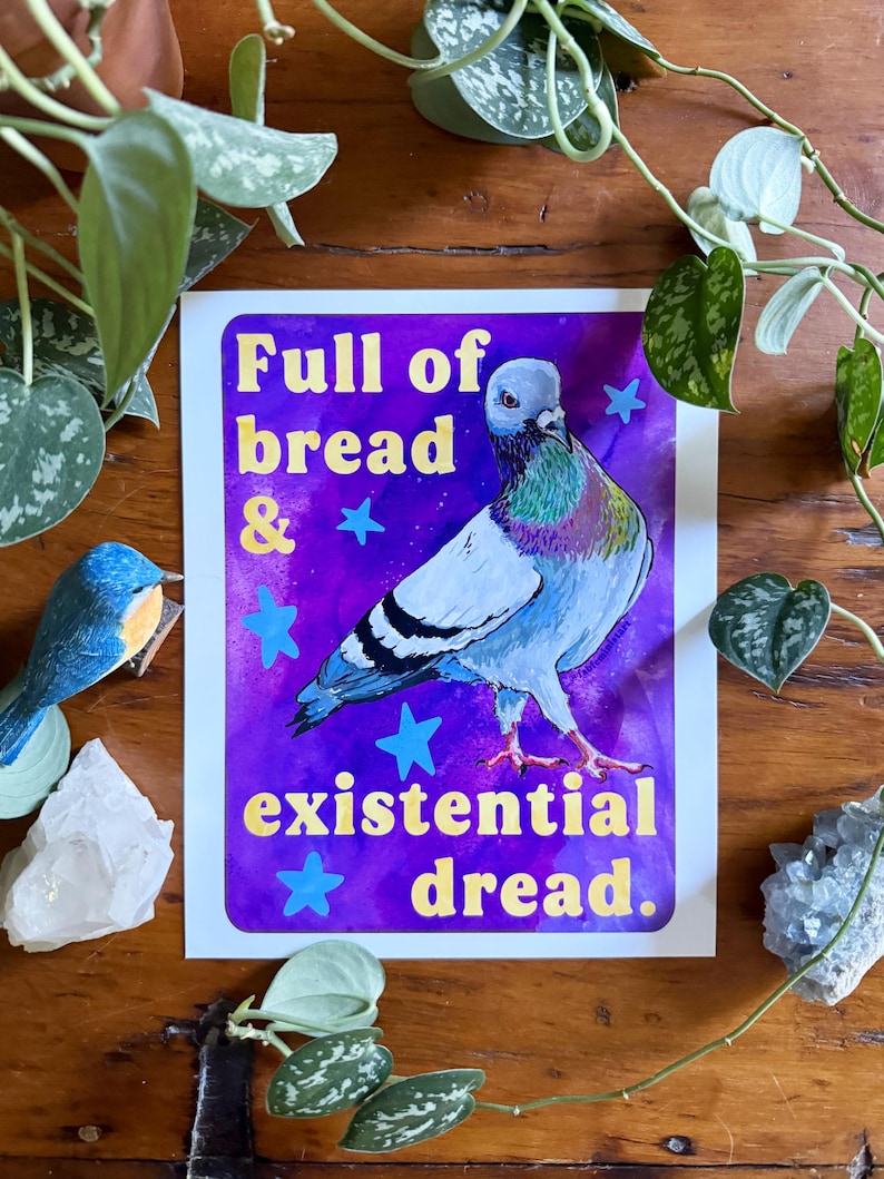 K&ouml;nnte beinhalten: Ein rechteckiger Kunstdruck mit einem Taubenmotiv vor einem leuchtend violetten Hintergrund mit blauen Sternen. Der Text lautet Full of bread & existential dread. Die Taube hat graue, wei&szlig;e und schillernd gr&uuml;ne Federn. Der Druck hat abgerundete Ecken.