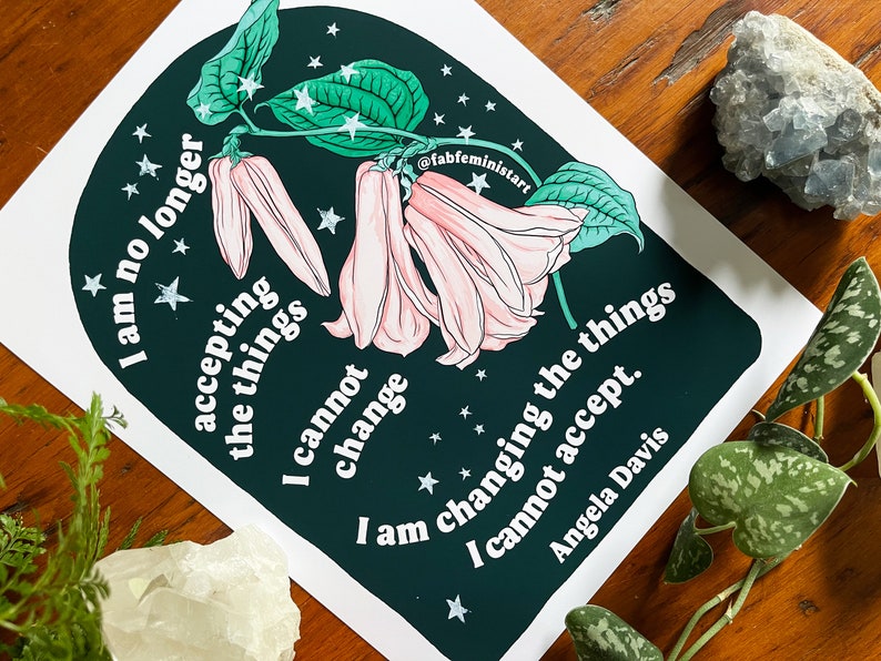 May include: A dark green print featuring a pink flower and white stars. The print includes the quote "I am no longer accepting the things I cannot change. I am changing the things I cannot accept." by Angela Davis.