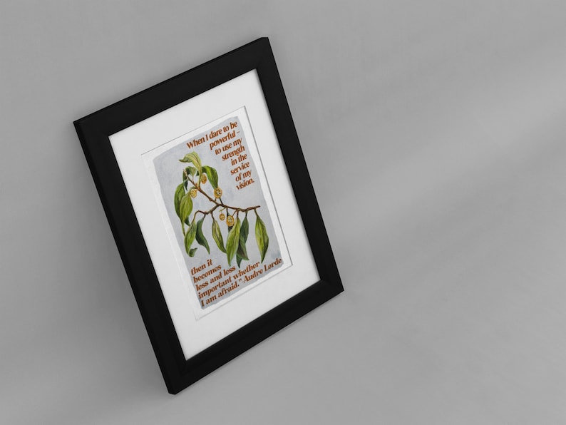 K&ouml;nnte beinhalten: Ein gerahmter Druck mit einer Aquarell-Illustration eines Zweigs mit gr&uuml;nen Bl&auml;ttern und kleinen orangen Fr&uuml;chten. Der Druck zeigt ein Zitat von Audre Lorde: "Wenn ich es wage, m&auml;chtig zu sein - meine St&auml;rke im Dienste meiner Vision einzusetzen, dann wird es immer weniger wichtig, ob ich Angst habe."