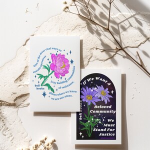 May include: Two cards with floral illustrations and text. The first card features a pink flower with blue stars and the text "One of the most vital ways we sustain ourselves is by building communities of resistance. Places where we know we are not alone." The second card features a purple flower with blue stars and the text "If we want a Beloved Community We Must Stand For Justice #blackfeministart".