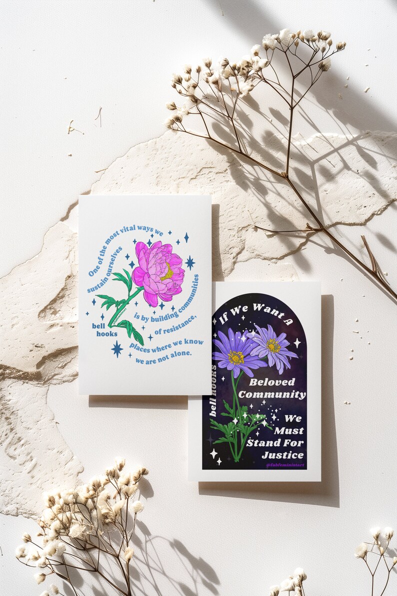 May include: Two cards with floral illustrations and text. The first card features a pink flower with blue stars and the text "One of the most vital ways we sustain ourselves is by building communities of resistance. Places where we know we are not alone." The second card features a purple flower with blue stars and the text "If we want a Beloved Community We Must Stand For Justice #blackfeministart".
