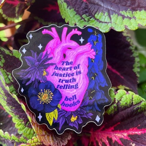 Puede incluir: Una pegatina con una ilustraci&oacute;n de coraz&oacute;n anat&oacute;mico rosa rodeada de flores moradas y una cita que dice "El coraz&oacute;n de la justicia es decir la verdad bell hooks".