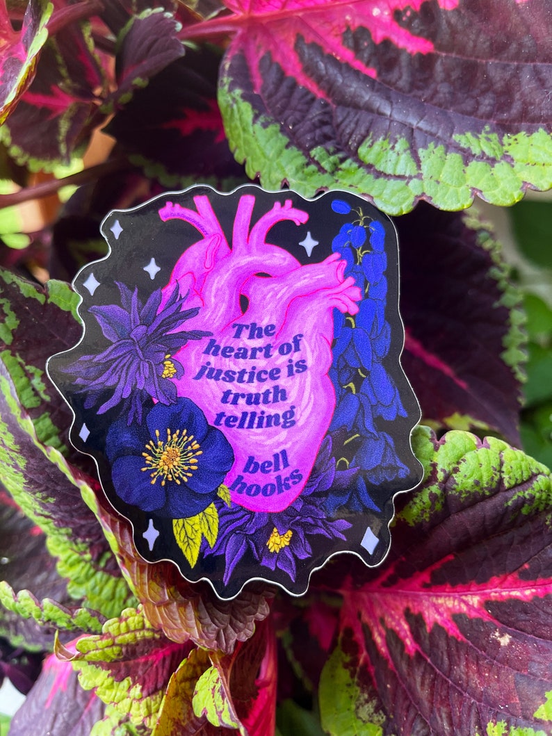 Puede incluir: Una pegatina con una ilustraci&oacute;n de coraz&oacute;n anat&oacute;mico rosa rodeada de flores moradas y una cita que dice "El coraz&oacute;n de la justicia es decir la verdad bell hooks".