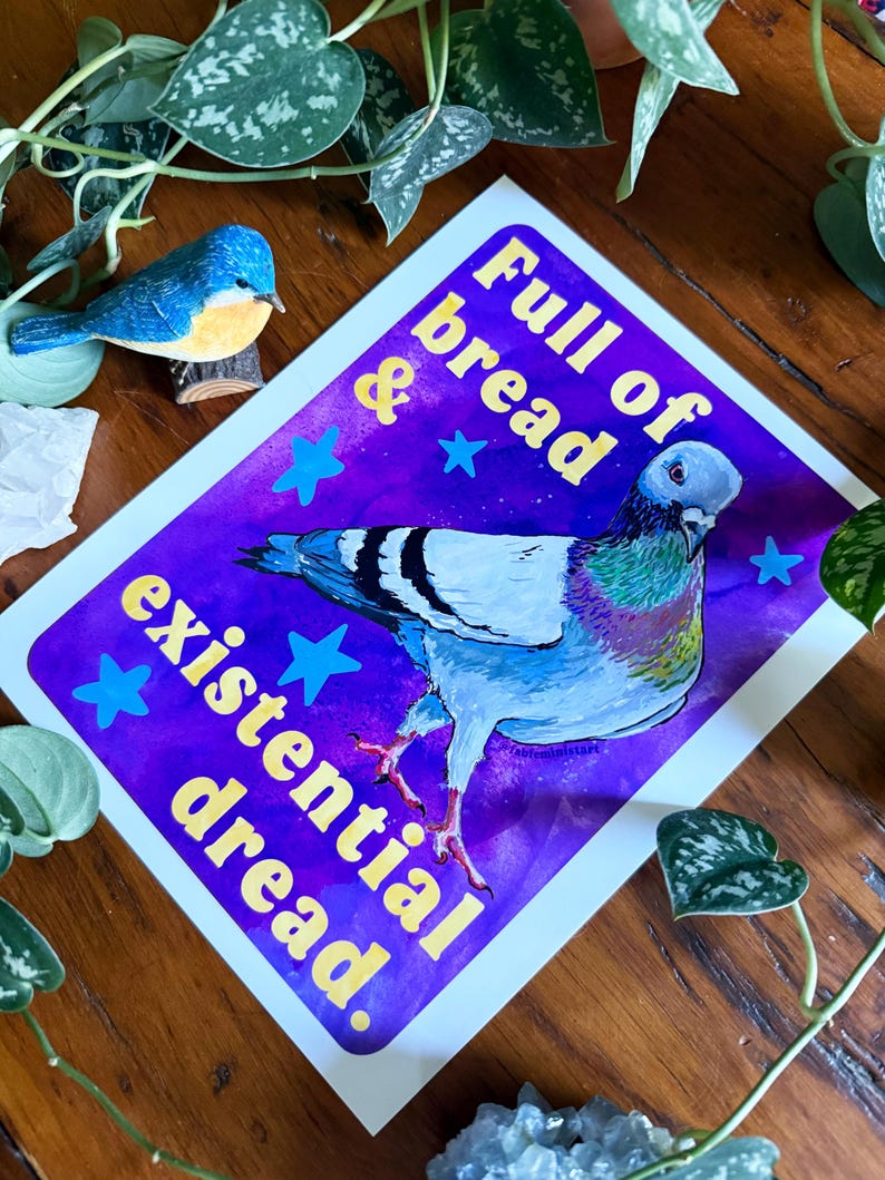 K&ouml;nnte beinhalten: Ein rechteckiger Kunstdruck mit einer Taube vor einem violett-blauen Galaxie-Hintergrund mit hellblauen Sternen. Der Text lautet Full of bread & existential dread in gelben Buchstaben. Die Taube hat graue, wei&szlig;e und schillernd gr&uuml;ne Federn.
