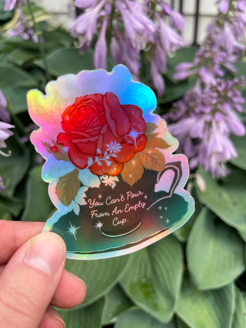 May include: A holographic sticker with a red rose in a teacup. The sticker has the text "You Can't Pour From An Empty Cup."