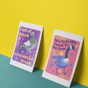 K&ouml;nnte beinhalten: Zwei rechteckige Kunstdrucke. Der linke Druck zeigt eine Taube auf violettem Hintergrund mit dem Text Full of bread & existential dread. Der rechte Druck zeigt eine Gans auf rosa Hintergrund mit dem Text Born To Be Silly Forced To Pay Taxes.