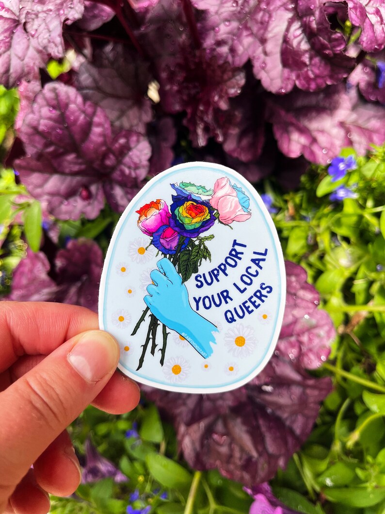 May include: A blue and white sticker with a rainbow rose bouquet and the text "Support Your Local Queers".