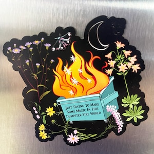 Könnte beinhalten: Ein schwarzer und blaugrüner Mülltonnenfeuer-Aufkleber mit einer Sichelmond, einem Schmetterling und Blumen. Der Text auf dem Aufkleber lautet "Just trying to make some magic in this dumpster fire world."