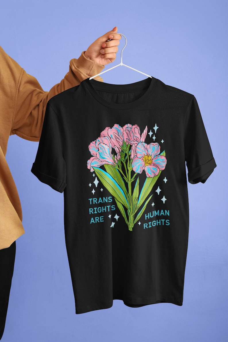 Puede incluir: Camiseta negra con un gr&aacute;fico de flores rosa y azul y el texto "Trans Rights Are Human Rights".