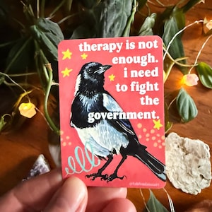 May include: A rectangular sticker with a pink background featuring a black and white bird illustration. Text reads "therapy is not enough. I need to fight the government." Yellow stars and teal swirls accent the design.