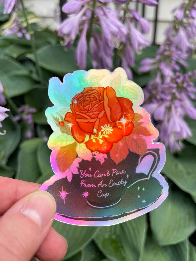 May include: A holographic sticker with a rose in a teacup. The sticker has a rainbow iridescent finish and features the text "You Can't Pour From An Empty Cup."