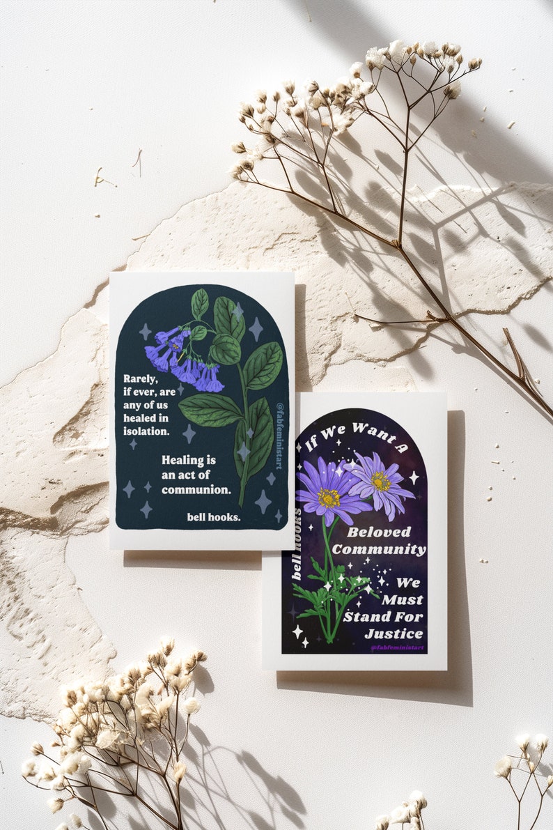May include: Two illustrated cards with a dark blue background and white text. The first card features a purple flower with green leaves and the text "Rarely, if ever, are any of us healed in isolation. Healing is an act of communion. bell hooks." The second card features a purple flower with green leaves and the text "If We Want A Beloved Community We Must Stand For Justice."