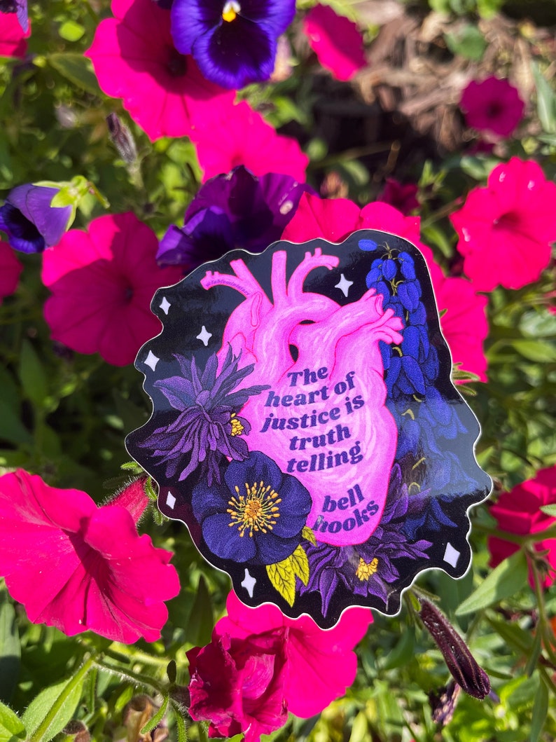Puede incluir: Una pegatina en forma de coraz&oacute;n rosa con fondo negro y detalles florales. La pegatina presenta la cita "El coraz&oacute;n de la justicia es decir la verdad" de bell hooks.