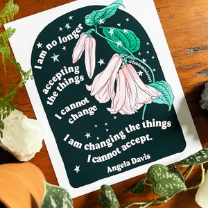May include: A dark green and black illustration of a flower with pink petals and white stars. The text "I am no longer accepting the things I cannot change. I am changing the things I cannot accept. Angela Davis" is written in white on the illustration.