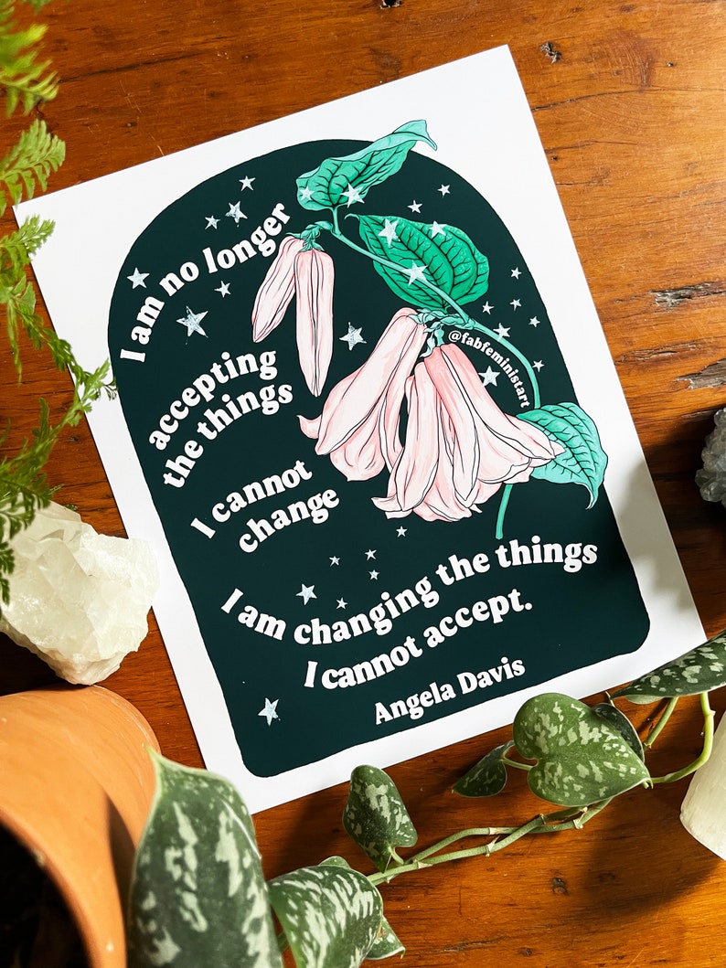 May include: A dark green and black illustration of a flower with pink petals and white stars. The text "I am no longer accepting the things I cannot change. I am changing the things I cannot accept. Angela Davis" is written in white on the illustration.