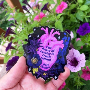 Puede incluir: Una pegatina en forma de coraz&oacute;n rosa con fondo negro y detalles florales. La pegatina presenta la cita "El coraz&oacute;n de la justicia es decir la verdad" de bell hooks.