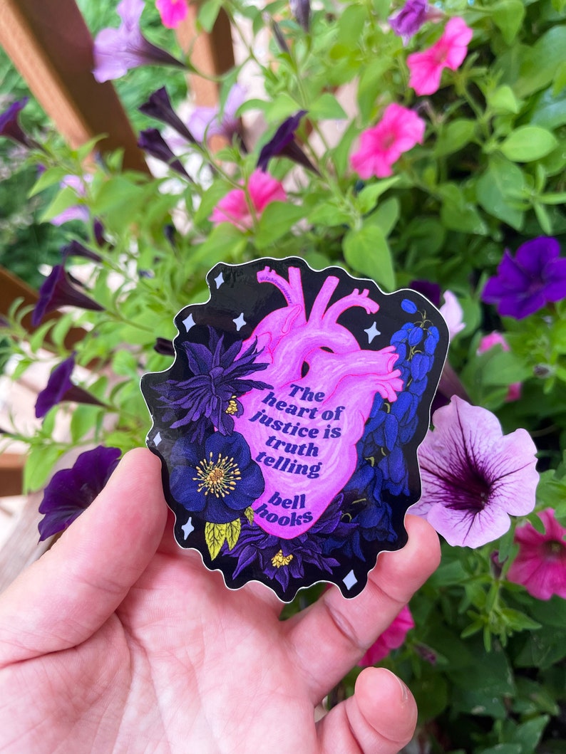 Puede incluir: Una pegatina en forma de coraz&oacute;n rosa con fondo negro y detalles florales. La pegatina presenta la cita "El coraz&oacute;n de la justicia es decir la verdad" de bell hooks.