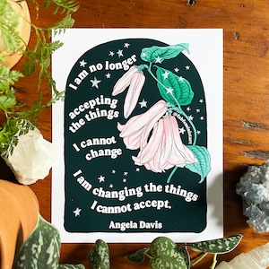May include: A dark green and black illustration of a flower with pink petals and white stars. The text "I am no longer accepting the things I cannot change. I am changing the things I cannot accept. Angela Davis" is written in white on the illustration.