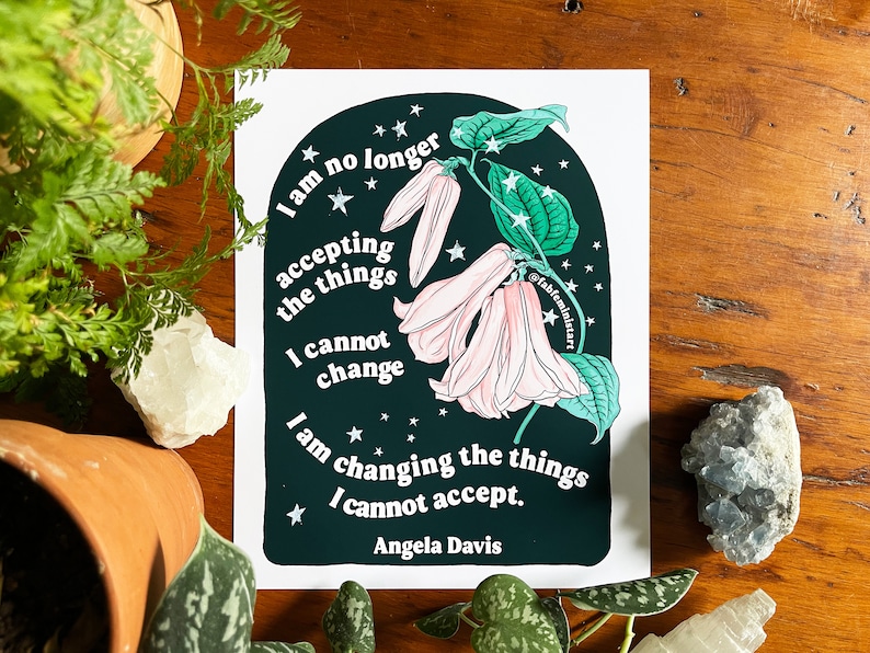 May include: A dark green and black illustration of a flower with pink petals and white stars. The text "I am no longer accepting the things I cannot change. I am changing the things I cannot accept. Angela Davis" is written in white on the illustration.
