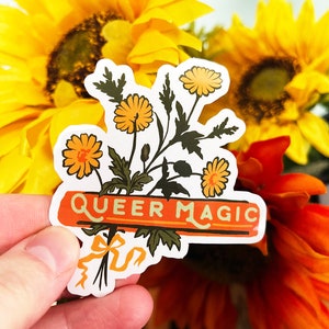 Puede incluir: Una pegatina con un ramo de flores amarillas y una pancarta que dice "Queer Magic". La pegatina se sostiene en una mano sobre un fondo de girasoles.