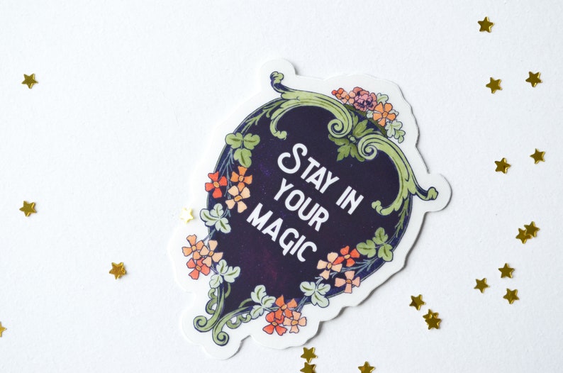 May include: A sticker with a dark blue background and white text that reads "Stay in your magic". The sticker is surrounded by a green and gold floral design.