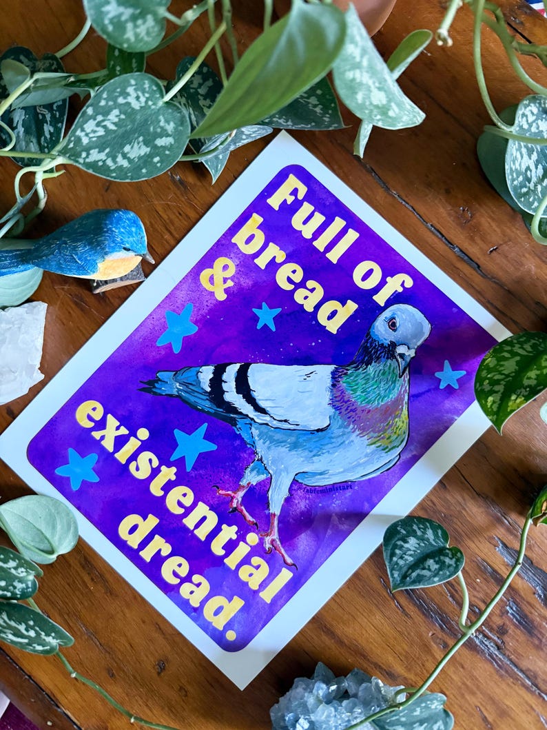 K&ouml;nnte beinhalten: Ein rechteckiger Kunstdruck mit einem Taubenmotiv vor einem leuchtend violetten und blauen Aquarellhintergrund. Der Text Full of bread & existential dread steht in gelben Buchstaben, umgeben von kleinen blauen Sternen.