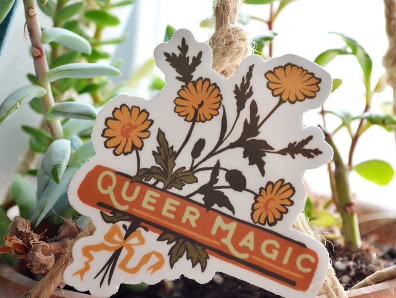 Puede incluir: Una pegatina con un ramo de flores amarillas y una pancarta que dice "Queer Magic".