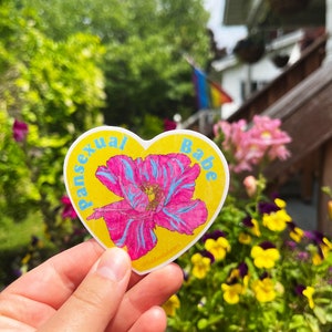 May include: A yellow heart-shaped sticker with a pink and blue flower and the text "pansexual babe".