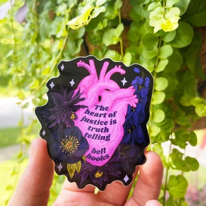 Puede incluir: Una pegatina de coraz&oacute;n anat&oacute;mico rosa con detalles florales negros y la cita "El coraz&oacute;n de la justicia es decir la verdad, bell hooks" sobre un fondo negro.
