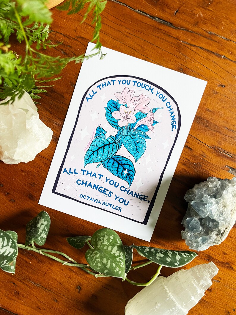 Peut inclure: Une impression rose et bleue avec une citation d'Octavia Butler : "Tout ce que vous touchez, vous changez. Tout ce que vous changez, vous change."
