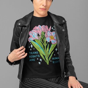 Puede incluir: Camiseta negra con un gr&aacute;fico de flores rosa y azul y el texto "Trans Rights Are Human Rights".
