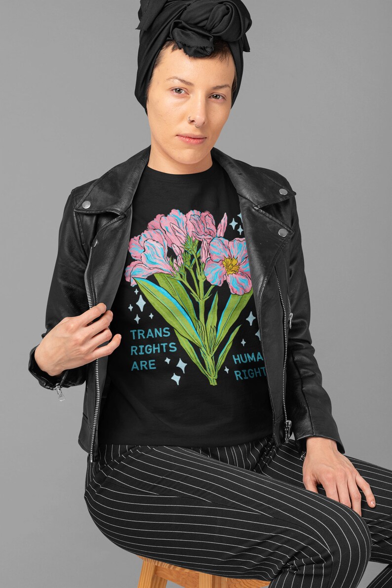 Puede incluir: Camiseta negra con un gr&aacute;fico de flores rosa y azul y el texto "Trans Rights Are Human Rights".