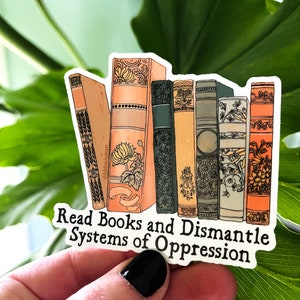 May include: A sticker with a stack of illustrated books and the text "Read Books and Dismantle Systems of Oppression".