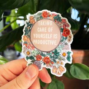 May include: A white sticker with a floral border and a pink circle in the centre. The text inside the circle reads "Taking care of yourself is productive."