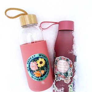 May include: Two pink water bottles with different designs. The bottle on the left has a sticker with flowers and the text "We repeat what we don't repair". The bottle on the right has a sticker with flowers and the text "Taking care of yourself is productive".
