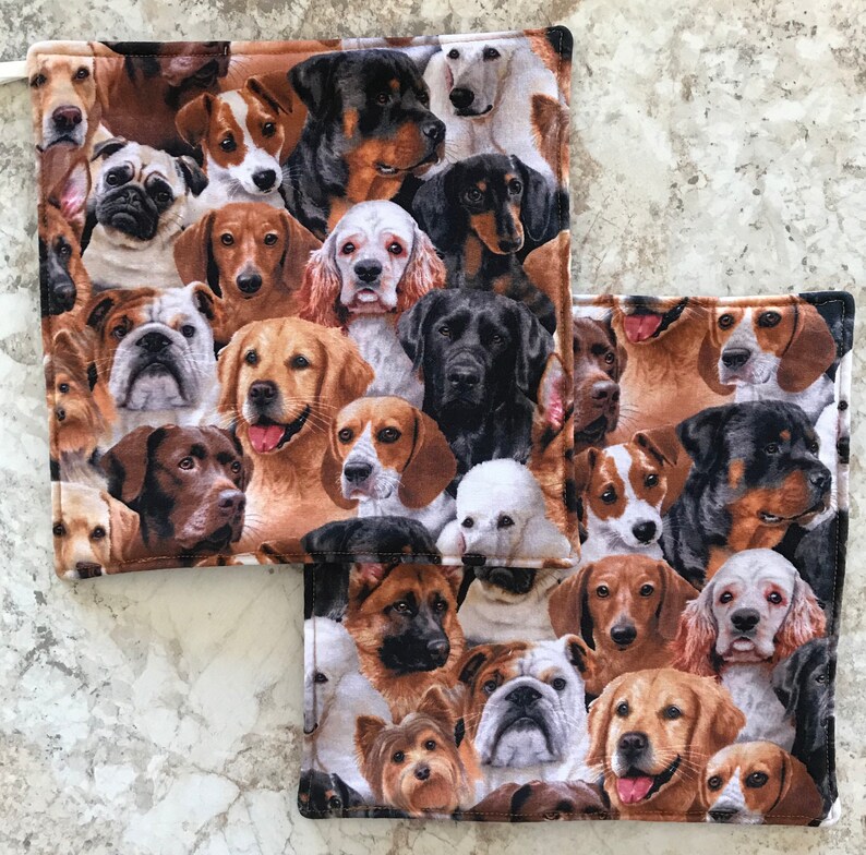 May include: A set of two brown and white fabric pot holders with a pattern of various dog breeds. The pot holders are square shaped and have a stitched border.