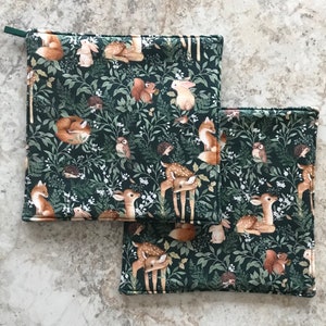 May include: Two green fabric pot holders with a woodland animal print. The print features deer, foxes, rabbits, squirrels, and birds on a dark green background.