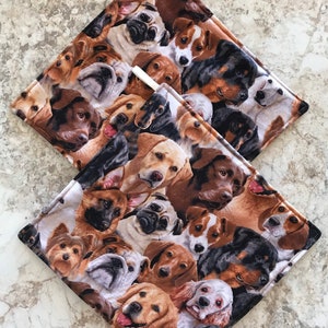 May include: Two brown and white pot holders with a pattern of various dog breeds. The pot holders are made of fabric and have a white loop for hanging.