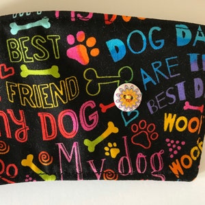 May include: Black fabric coffee cup sleeve with colorful text and dog-themed graphics. The text includes "Best Friend," "My Dog," and "Dog Day." A button with a floral design secures the sleeve.