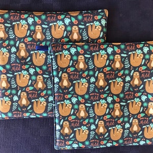 May include: Two brown and black pot holders with a repeating pattern of sloths hanging from branches. The sloths are brown with light brown fur. The background is dark blue with green leaves and orange flowers. The text "Born to be Mild" is repeated throughout the pattern.