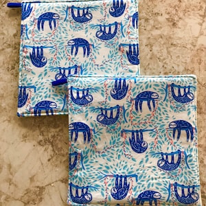 Peut inclure: Deux maniques en coton bleu et blanc avec un motif de paresseux. Les paresseux sont suspendus à des branches avec des feuilles bleues. Les maniques ont une bordure bleue.